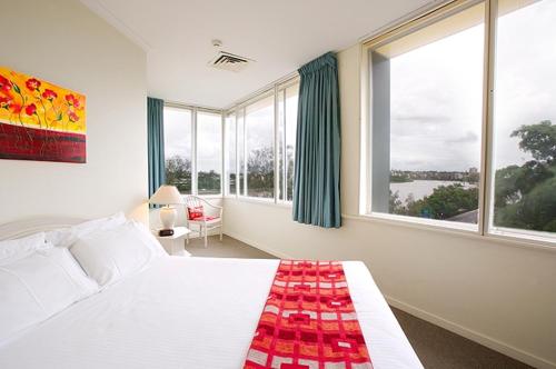 a bedroom with a large white bed with windows at Chasely Apartment Hotel in Brisbane