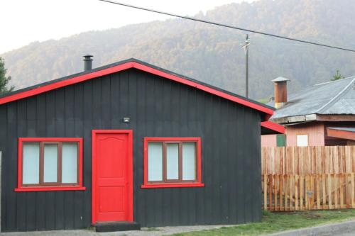 a black house with red windows and a red door at Refugio Simple Sur Casa 4 - 5 personas in Malalcahuello