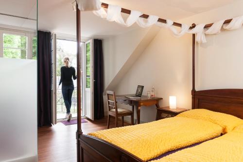a woman walking into a bedroom with a bed and a desk at Kulturhotel Guggenheim in Liestal