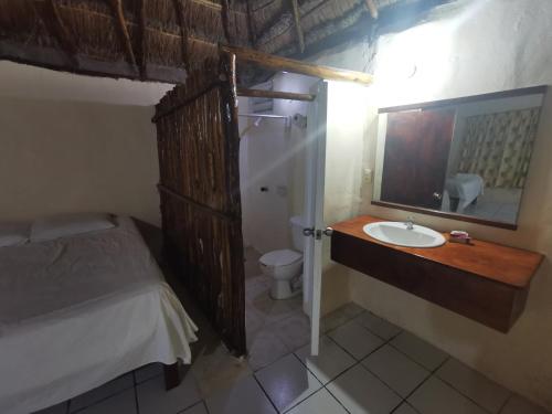 baño con lavabo, cama y espejo en Las Cabañas del Doctor, en Mahahual