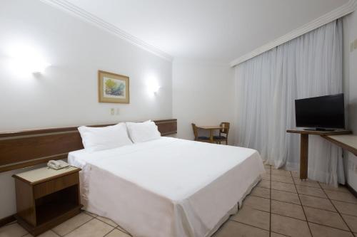 a bedroom with a large white bed and a television at Catussaba Resort Hotel in Salvador