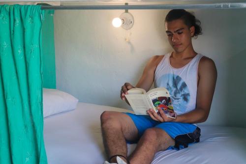 a man sitting on a bed reading a book at Wabi Hostel in Playa del Carmen