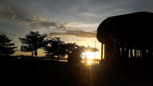 a sun setting behind some trees and a building at Houttuyn Wellness River Resort in Paramaribo