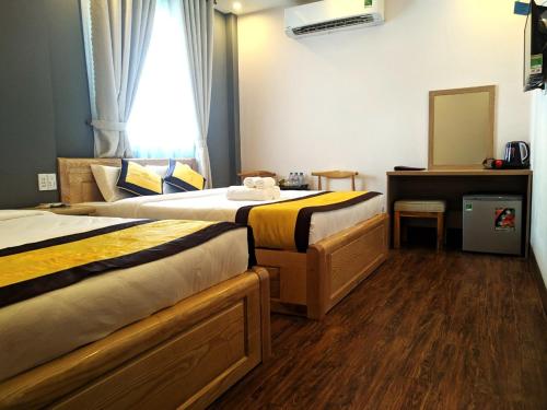 a bedroom with two beds and a desk and a window at Hoàng Gia Hotel Côn Đảo in Con Dao