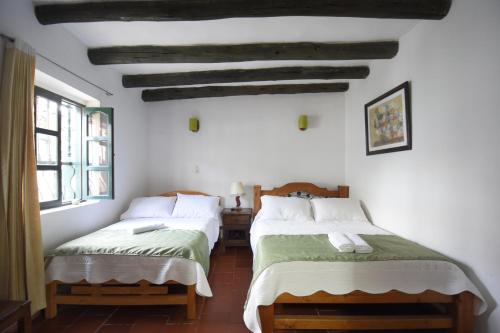 two beds in a room with white walls at Hospederia La Fuente in Villa de Leyva