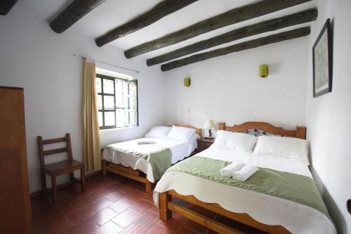 a bedroom with two beds and a chair at Hospederia La Fuente in Villa de Leyva