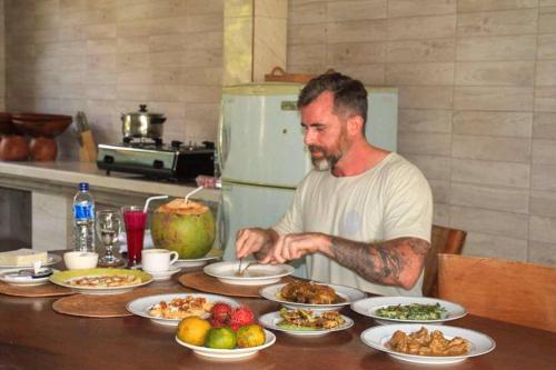 a man sitting at a table with plates of food at Arsa Wayan Guest House in Klungkung