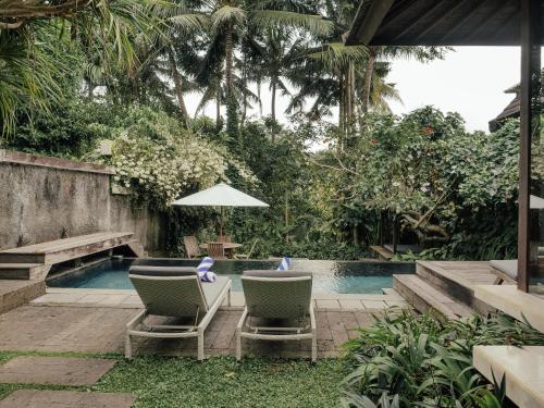 two chairs and an umbrella next to a swimming pool at Surya Kembar Villas in Ubud