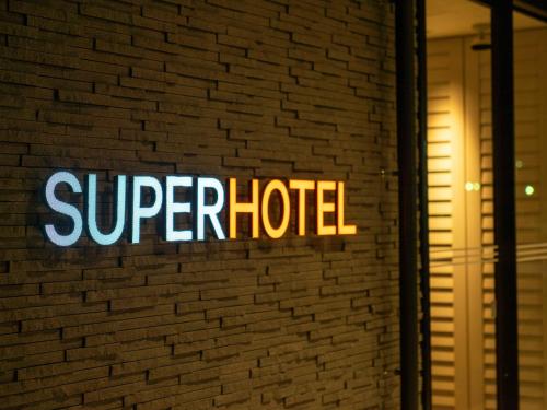 a sign for a super hotel on a brick wall at Super Hotel Anan Tomioka in Anan