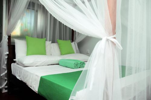 ein Bett mit grünen und weißen Kissen und einem Baldachin in der Unterkunft Villa Serenity - Jayavikumgama in Weligama