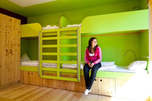 a woman sitting on a bed in a room with bunk beds at Jugendherberge Berchtesgaden in Berchtesgaden
