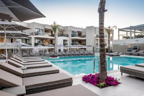 a pool with chairs and a palm tree in front of a building at Porto Platanias Beach Luxury Selection - Adults Only in Plataniás