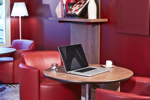 a laptop sitting on a table in a room with red chairs at Campanile Le Havre Nord - Montivilliers in Montivilliers