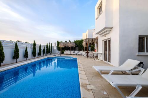 a swimming pool with white chairs and a building at Thalassines Villas in Ayia Napa
