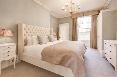 a white bedroom with a large bed and a chandelier at Stunning Montpellier Spa Road apartment in Cheltenham