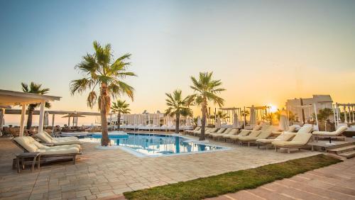 a swimming pool with lounge chairs and palm trees at Parthenis Beach, Suites by the Sea in Malia
