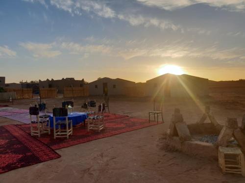 une table et des chaises dans le désert avec le coucher du soleil dans l'établissement Bivouac Mélodie du désert, à M'Hamid El Ghizlane