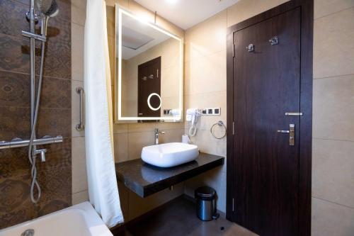 a bathroom with a sink and a mirror and a shower at Hotel Godwin - Colaba in Mumbai