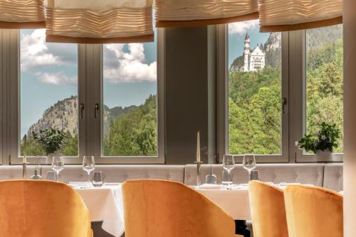 a table with chairs in a room with windows at AMERON Neuschwanstein Alpsee Resort & Spa in Schwangau