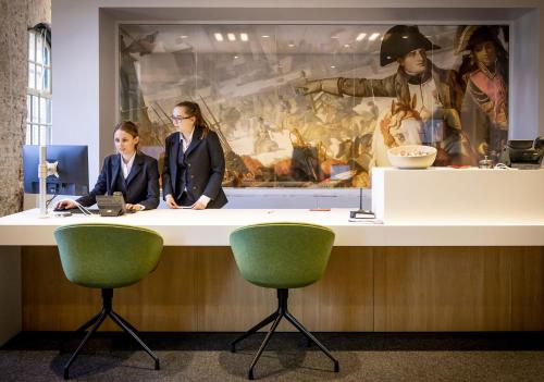 two women sitting at a counter in an office with a painting at Onderwijshotel De Rooi Pannen Breda in Breda