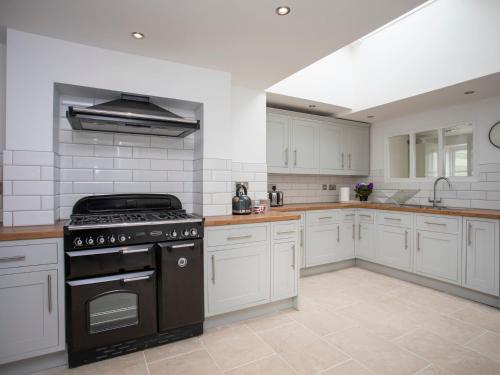 a kitchen with white cabinets and a black stove at Stabl Bach in Llanfaethlu