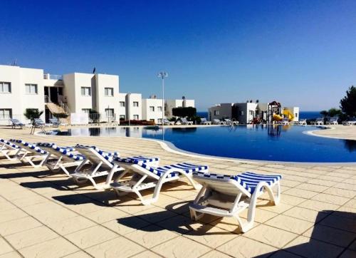 a row of lounge chairs in front of a swimming pool at The Seaterra Reserve Penthouse with mountains&seaviews and rooftop terrace in Akanthou