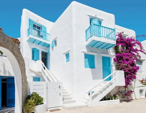 biały budynek z niebieskimi oknami i kwiatami w obiekcie Mykonian Mews Luxury Suites w mieście Psarrou