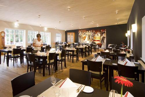 a woman standing in a dining room with tables and chairs at Heidehotel Gut Landliebe Restaurant Montags Ruhetag! in Hermannsburg