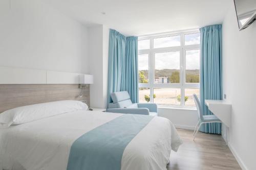 a bedroom with a bed and a chair and a window at Hostal Praia Madalena in Cedeira