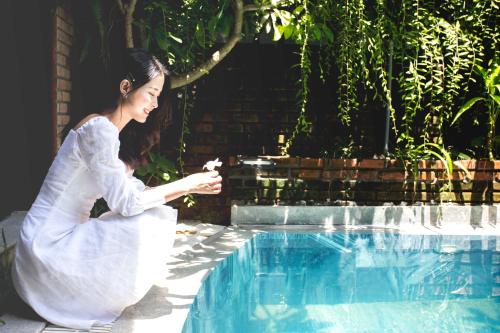 a woman in a white dress sitting next to a swimming pool at MAI Villa Da Nang in Da Nang