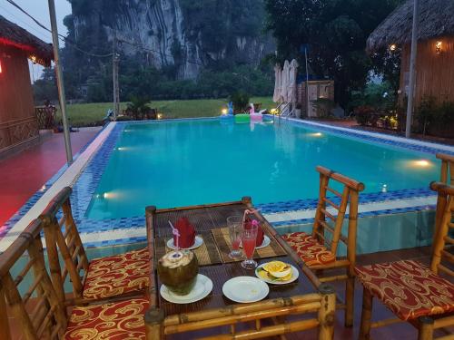 a table and chairs with a meal in front of a swimming pool at Tam Coc Horizon Bungalow in Ninh Binh
