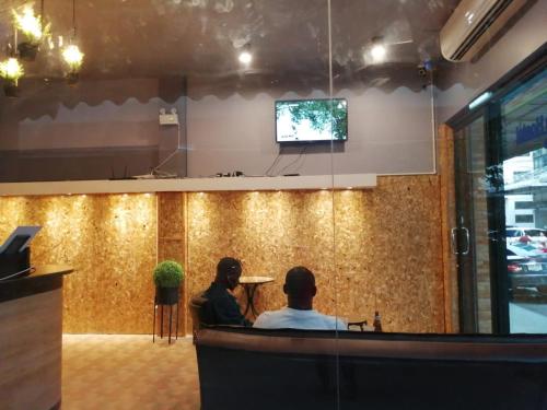 two people sitting at a bar watching a tv at SleepCatsHostel in Bangkok