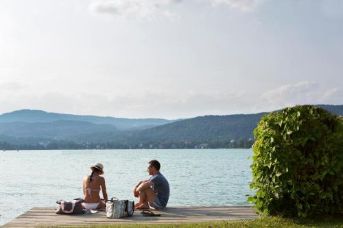 a man and woman sitting on a dock near the water at Hotel Linde in Maria Wörth