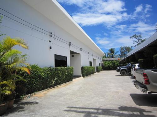 a white building with cars parked in a parking lot at Pine Home in Krabi town