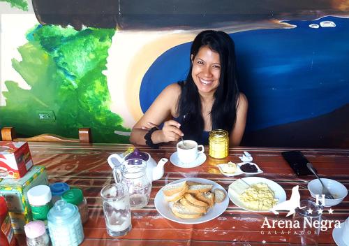 une femme assise à une table avec une assiette de nourriture dans l'établissement Hostal Arena Negra, à Puerto Ayora