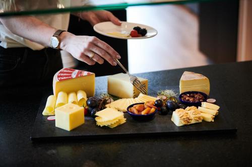 a person cutting cheese on a table with a plate of food at Hotel Holiday Thun in Thun