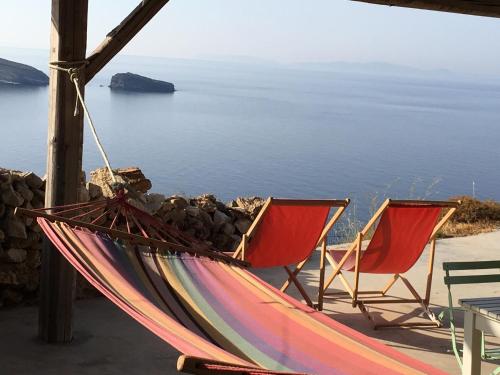 a hammock and two chairs sitting next to the ocean at Scorpio house 180 sea view - Serifians Residences in Serifos Chora