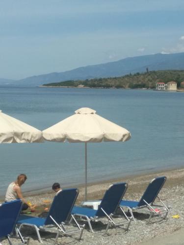two people sitting in chairs under an umbrella on the beach at Kalama Apartments in Kálamos