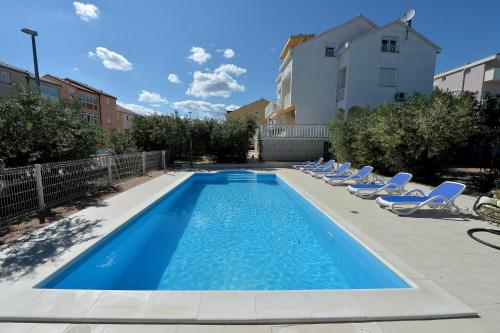 une piscine avec des chaises longues et un bâtiment dans l'établissement Apartments Olive Garden - swimming pool, à Biograd na Moru