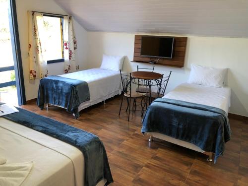 a room with two beds and a table and a tv at João e Maria Restaurante e Chalés in Tiradentes