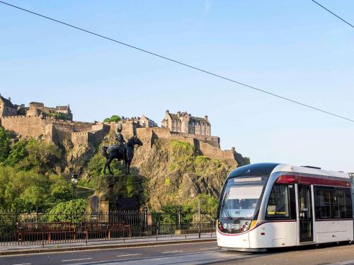 a bus driving down a street with a castle in the background at Novotel Edinburgh Park in Edinburgh