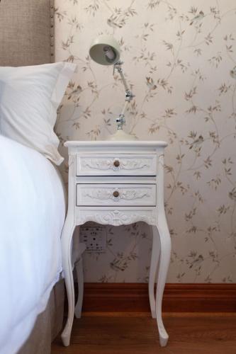 a white nightstand with a lamp on it next to a bed at Bella Blue Guesthouse in Bloemfontein