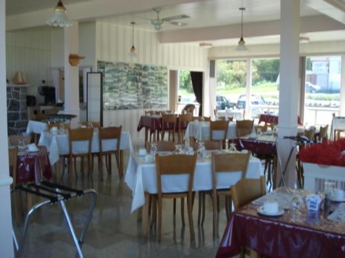 a dining room with white tables and chairs in a restaurant at Hôtel Motel du Rocher in Rivière-la-Madeleine