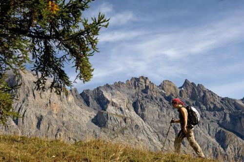 a man with a backpack walking in front of a mountain at Hôtel Les Bains d'Ovronnaz in Ovronnaz