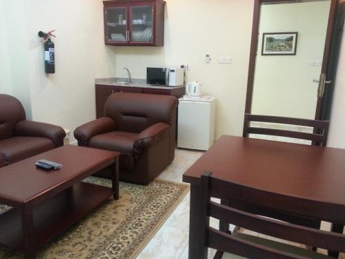 a living room with couches and tables and a kitchen at Al Ferdous Hotel Apartments in Muscat