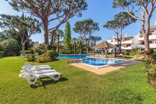 a group of white benches in the grass near a swimming pool at The Old Village, Prestige and Solar by Village 4U in Vilamoura