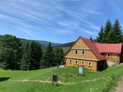 a house with a red roof on a green hill at Horská chalupa U Hančilů in Pec pod Sněžkou
