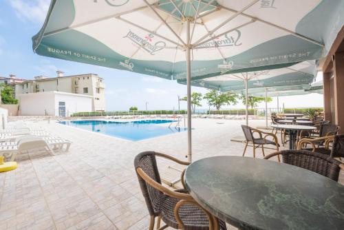 eine Terrasse mit einem Tisch mit einem Sonnenschirm und einem Pool in der Unterkunft Balchik Sea View Apartments in Princess Residence in Baltschik
