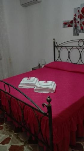 Una cama con una manta rosa y dos toallas. en A casa di Gio’, en Marsala
