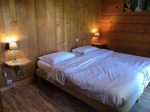 a bed in a wooden room with two lamps at La Ferme des Georgières "Séjour en tout compris" in Notre-Dame-de-Bellecombe